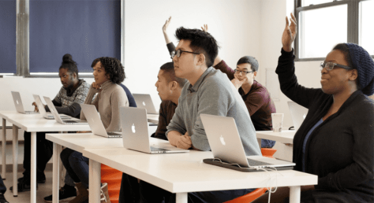 Galvanize students in a classroom with some raising their hands.