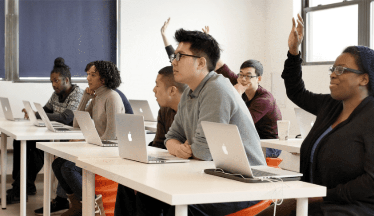 Galvanize students in a classroom with some raising their hands.