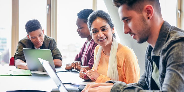 4 people talking at a desk with laptops