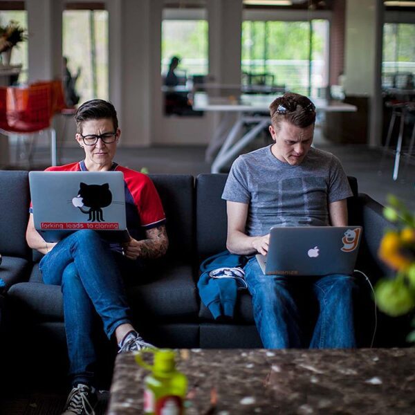 Two people working on their laptops on a couch together.