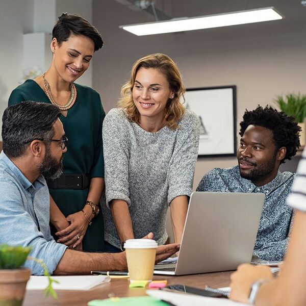 Two men and two women smiling while looking at a laptop screen.