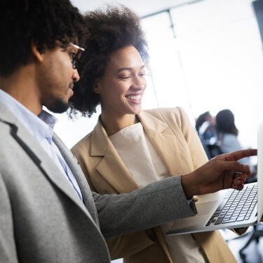 Man and woman smiling together looking at a laptop screen.