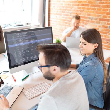 A man and woman working together to code on a laptop.