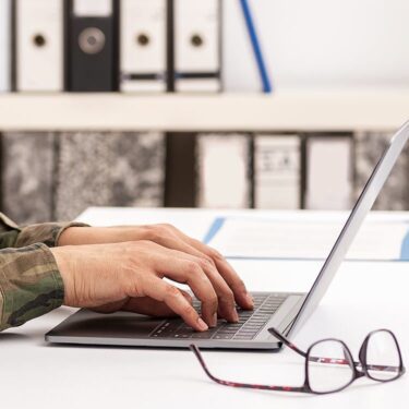 Military person typing on a laptop.