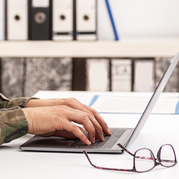 Military person typing on a laptop.