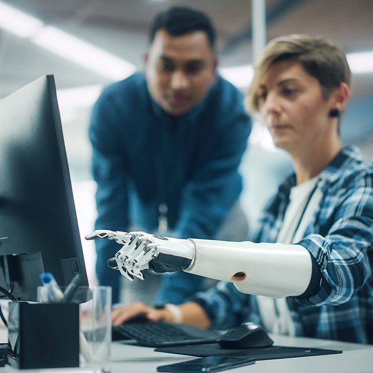 Man watching woman with prosthetic arm point to something on her computer monitor.