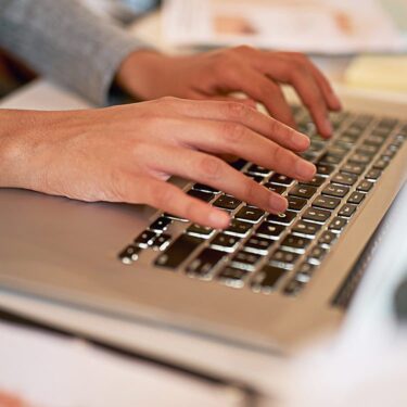 A persons hands typing on a laptop keyboard.